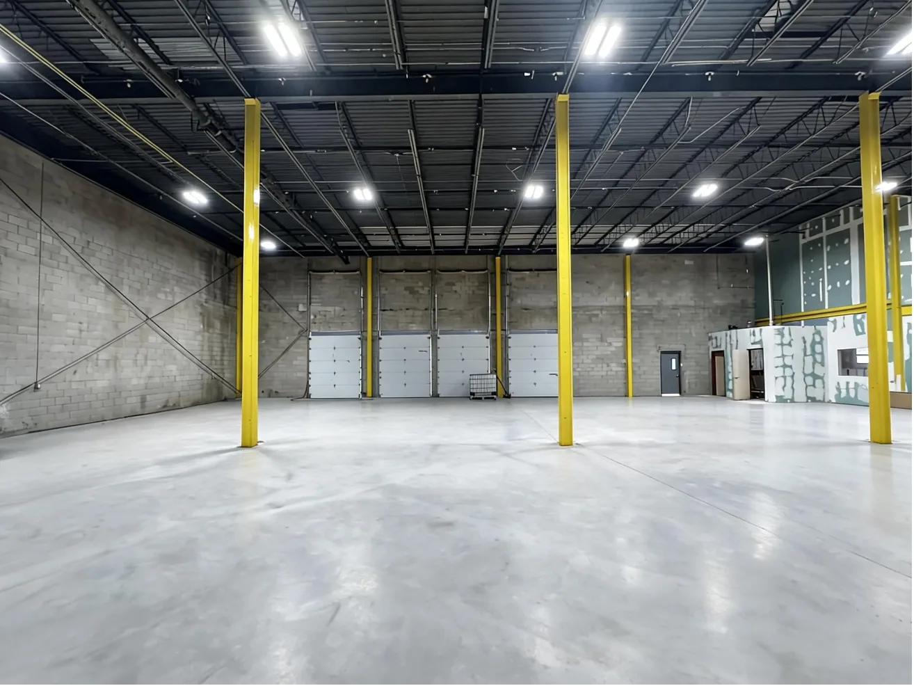 Inside 219 St Nicholas Avenue: open warehouse floor, yellow steel columns and four overhead doors